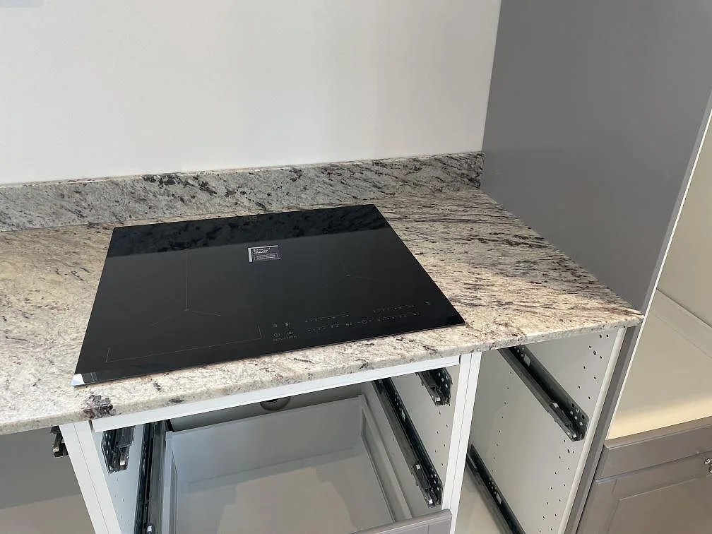 Köksbänkskiva i Antique White granit, polerad, med svart induktionshäll och öppna stommar i Klippan.