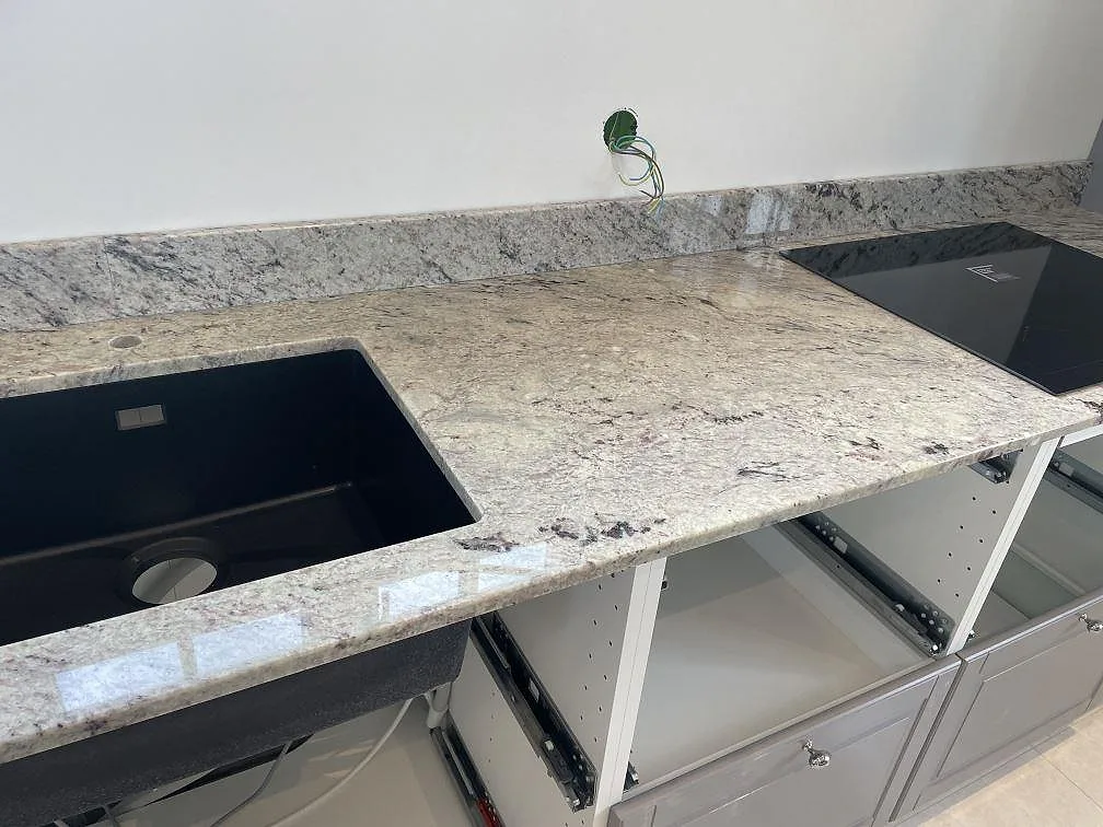 Polerad Antique White granit med svart diskho, svart induktionshäll och låg stänkkant i kök i Klippan.