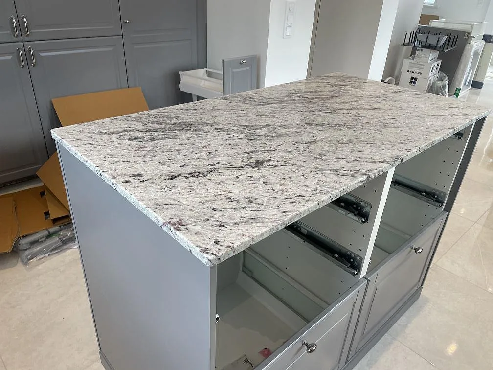 Halvö i polerad Antique White granit med grå skåp och synlig ljus stenstruktur i kök i Klippan.