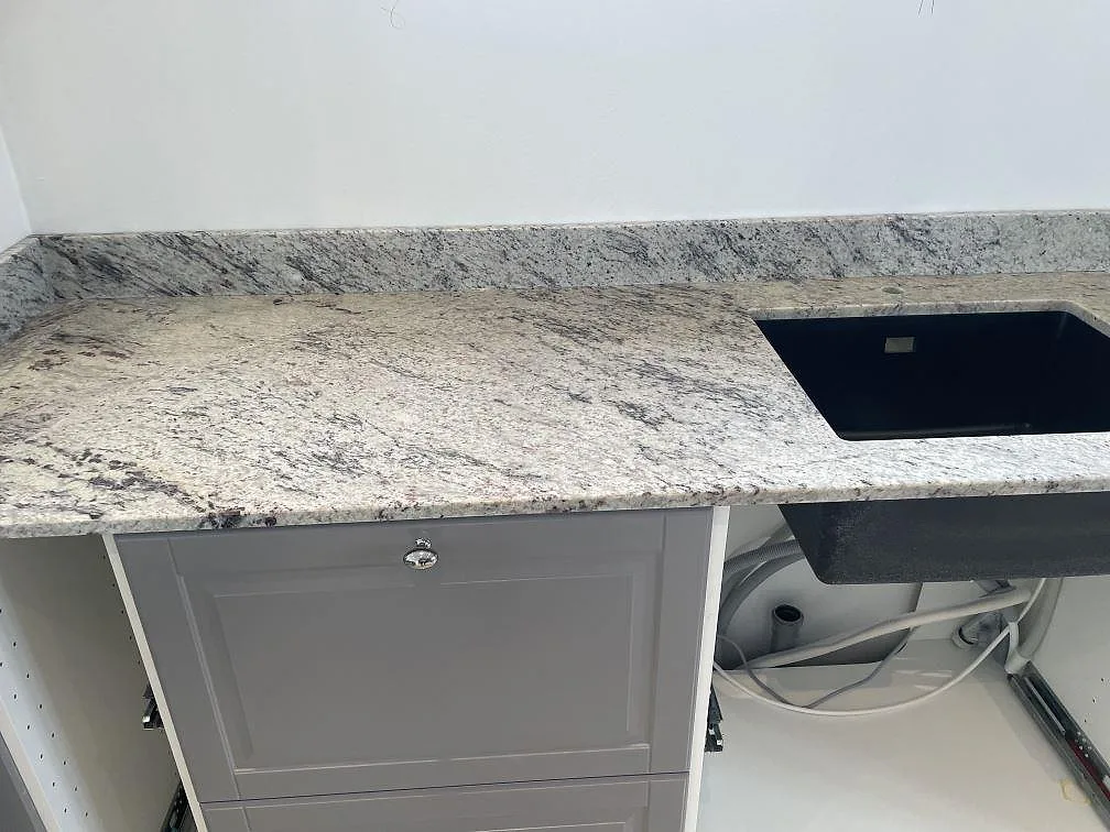 Närbild på polerad Antique White granit med svart diskho monterad under stenen och låg stänkkant i Klippan.