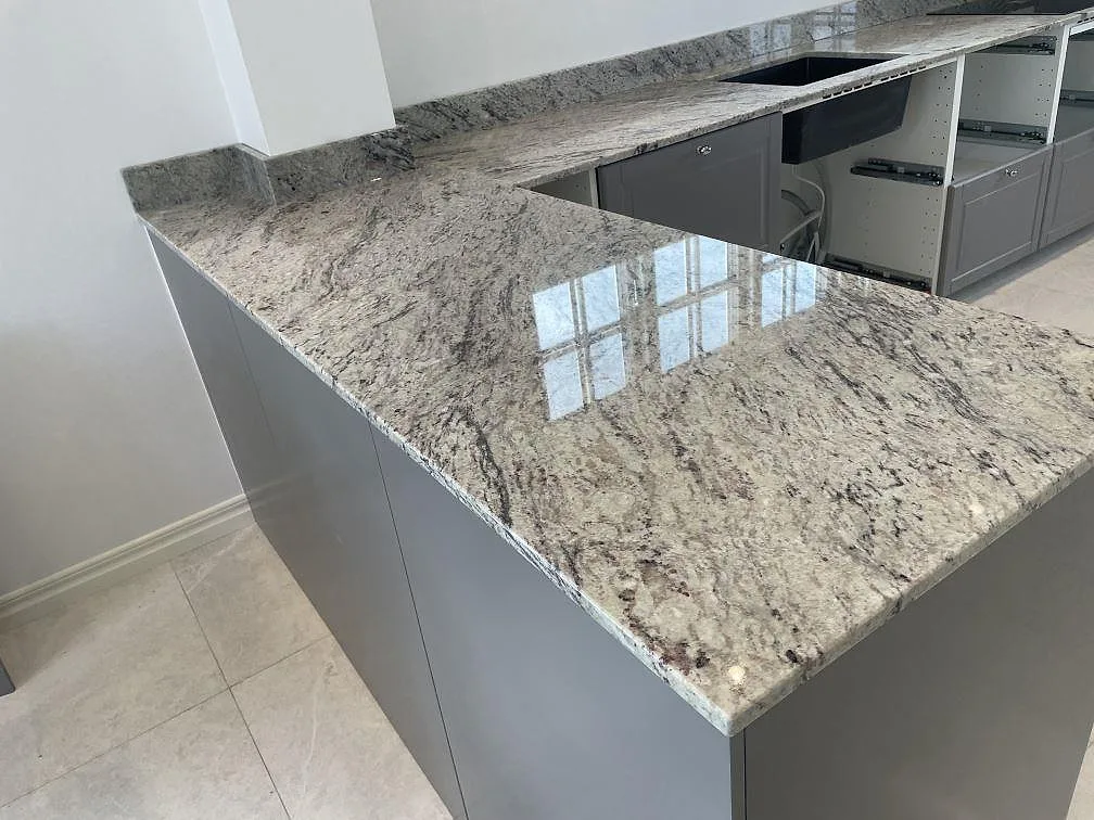 Polerad Antique White granit i U-format kök med halvö, låg stänkkant och svart underlimmad diskho i Klippan.