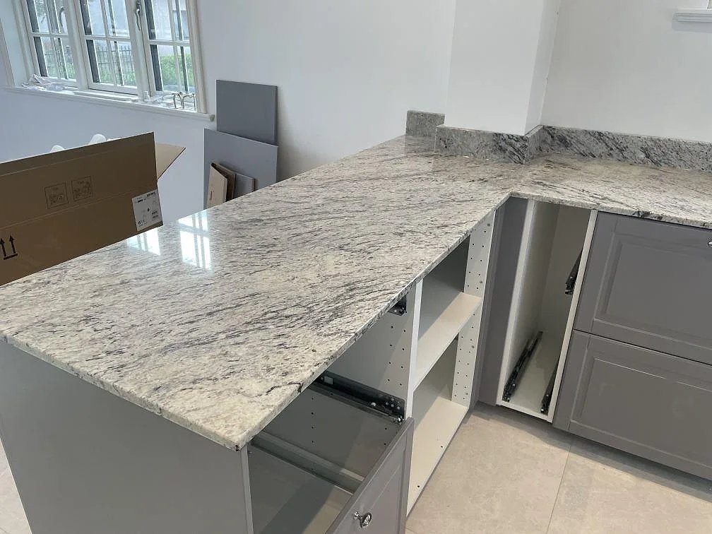 Köksbänkskiva i Antique White granit, polerad, med stor halvö och grå köksstommar vid fönster i Klippan.