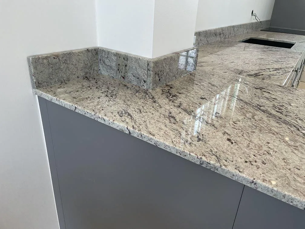 Närbild på polerad Antique White granit med låg stänkkant, svart diskho och ljus ådring i Klippan.