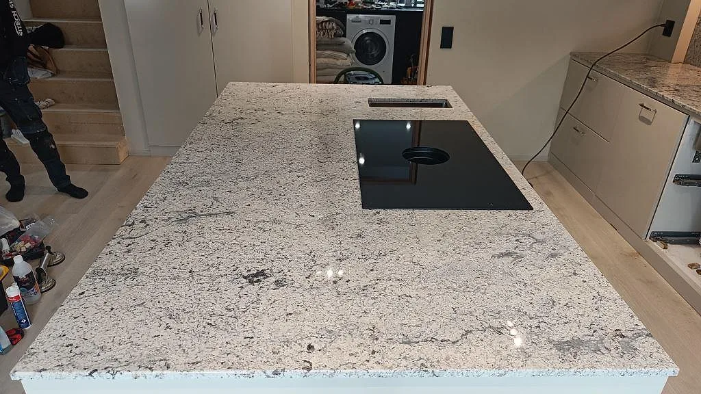 Köksö i mönstrad Antique White-granit med infälld induktionshäll under montering i ett kök i Kungsbacka.