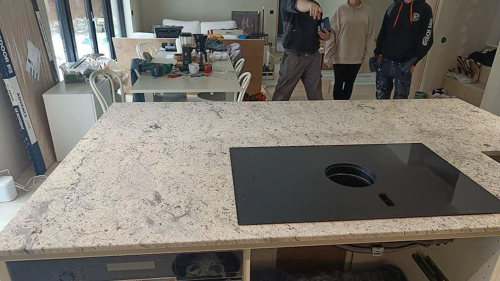 Köksö i Antique White-granit med induktionshäll sedd från matplatsen i ett kök under inredning i Kungsbacka.
