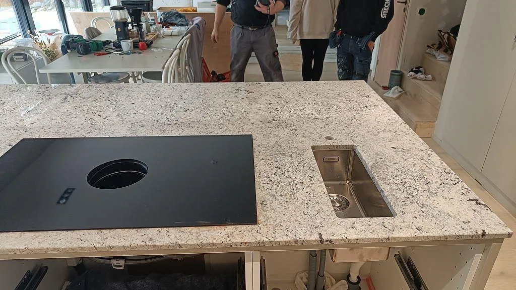 Detalj av underlimmad rostfri diskho och induktionshäll i en köksö av Antique White-granit i Kungsbacka.
