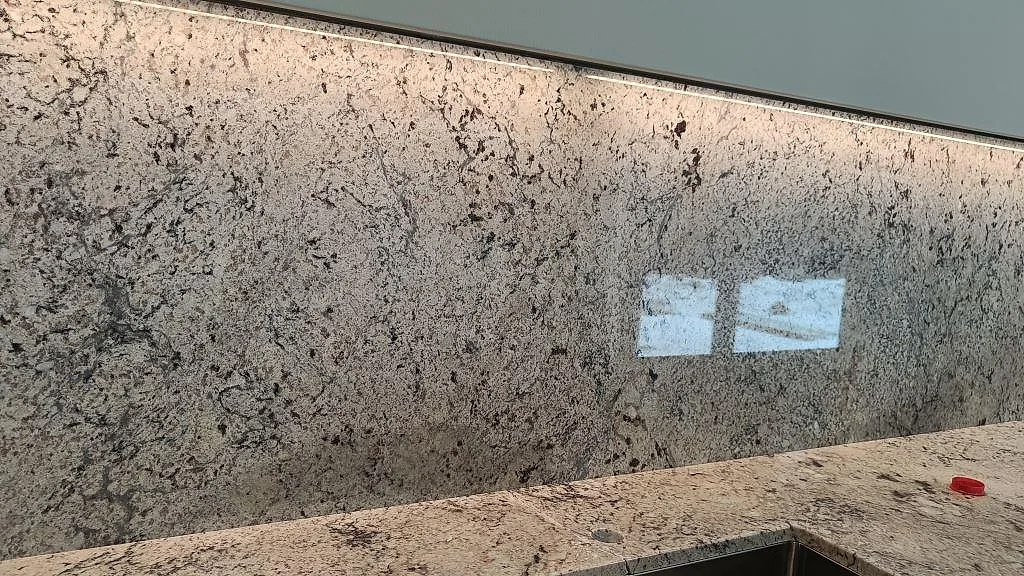 Bakbelyst stänkvägg i Antique White-granit med eluttag ovanför bänkskivan i ett kök i Kungsbacka.