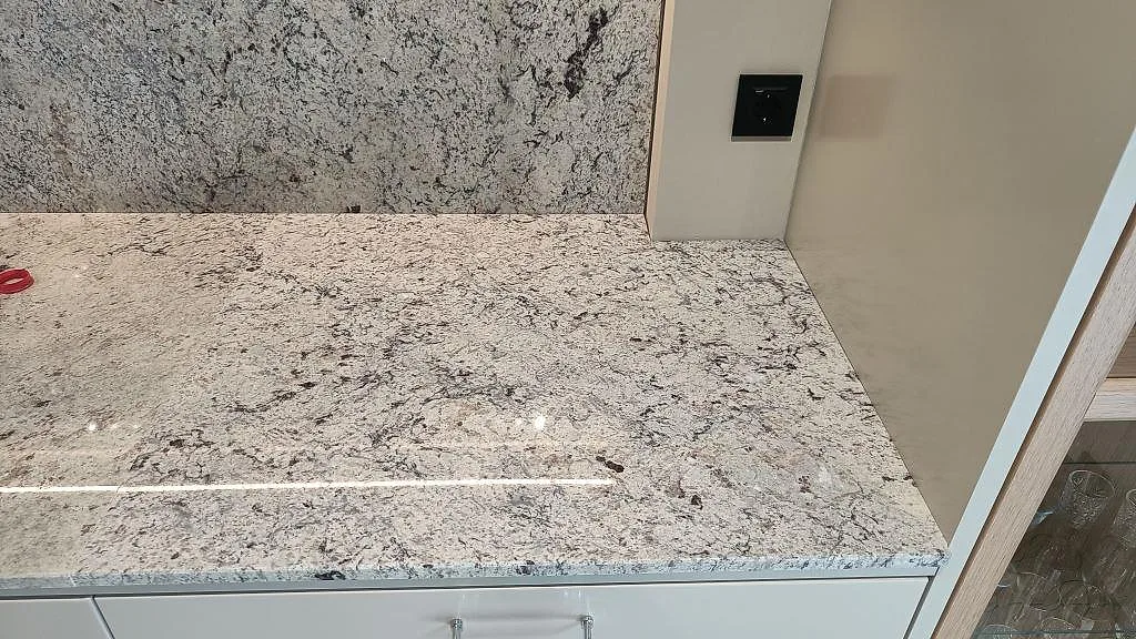 Bänkskiva i Antique White-granit mot en bakbelyst stänkvägg i samma sten i ett kök i Kungsbacka.