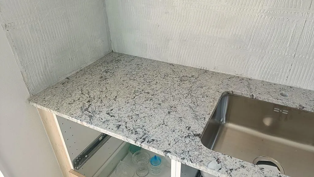 Underlimmad rostfri diskho infälld i polerad Antique White granitbänkskiva i ett kök i Landskrona.