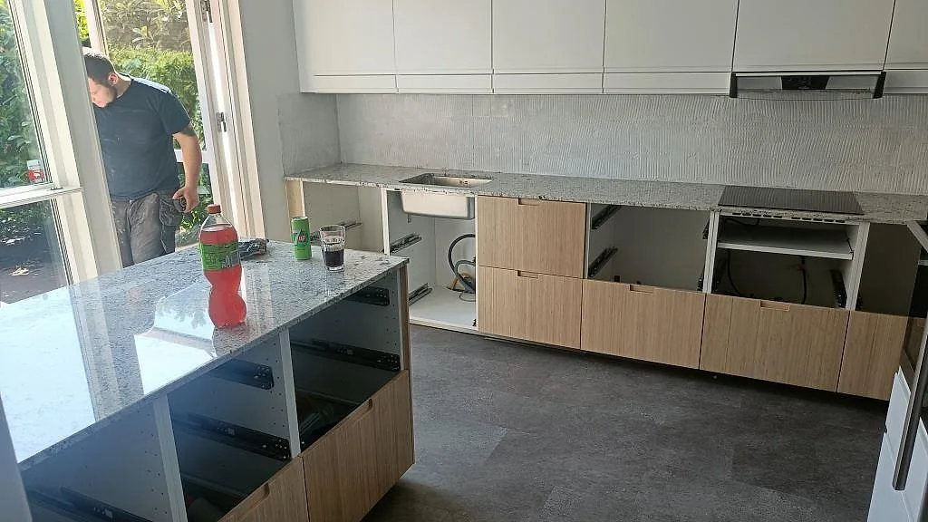 Köksbänkskiva i Antique White granit med köksö och underlimmad rostfri diskho i ett kök under montering i Landskrona.