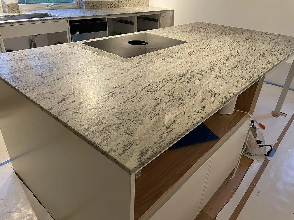Köksbänkskiva i matt Antique White granit, 20 mm, med svart induktionshäll och ljusgrå stommar i Landvetter.