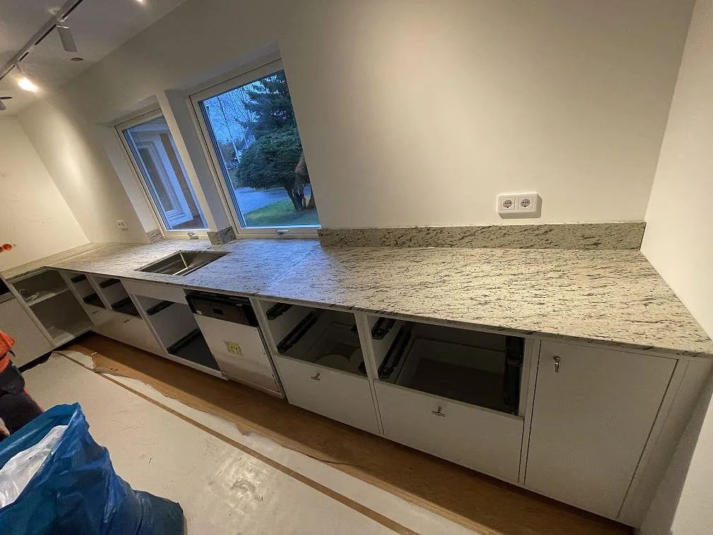 Lång köksbänkskiva i matt Antique White granit med underlimmad rostfri diskho, låg stänkkant och stora fönster i Landvetter.