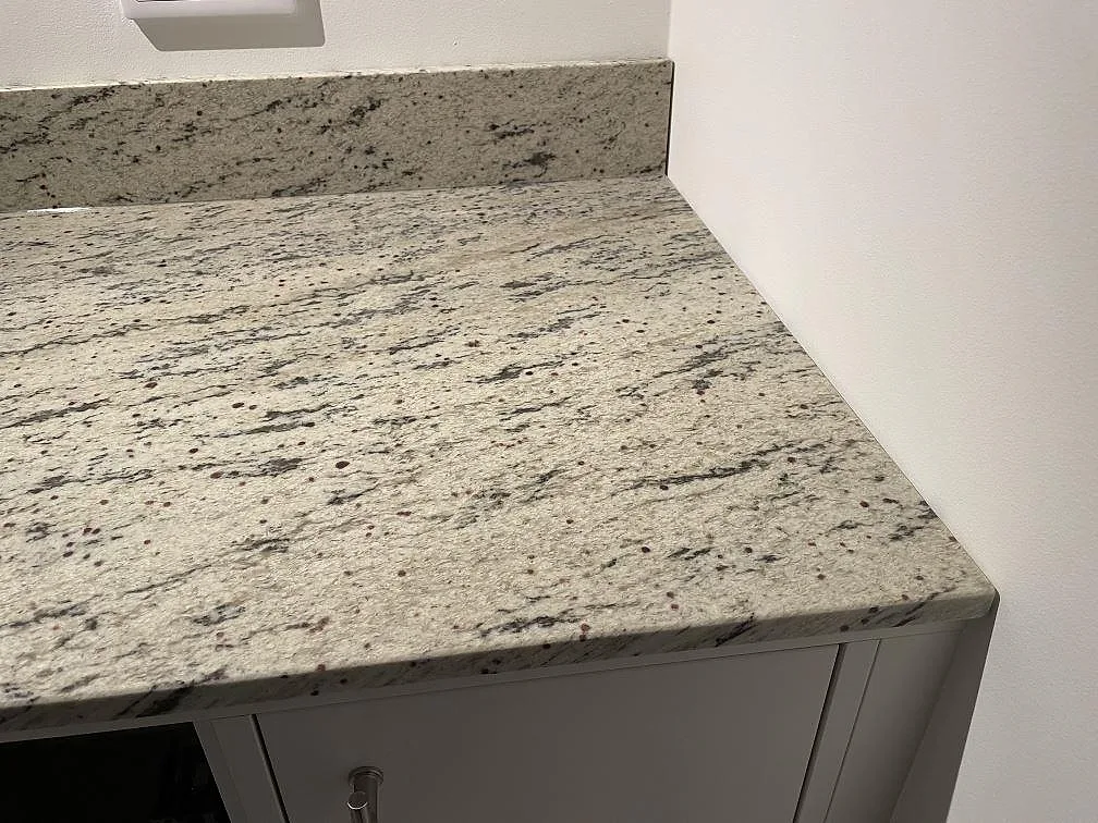 Detalj av matt Antique White granit med låg uppvikt stänkkant mot väggen i ett kök i Landvetter.