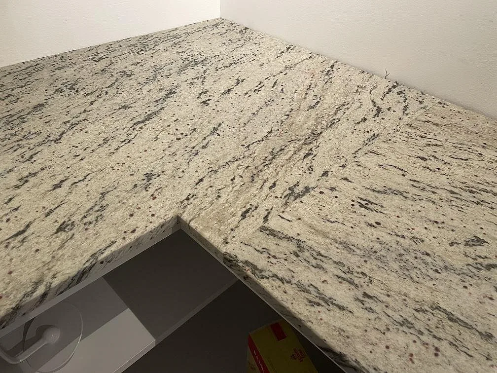 L-format hörn i matt Antique White granit med gråspräcklig yta och synlig 20 mm kant i köket i Landvetter.
