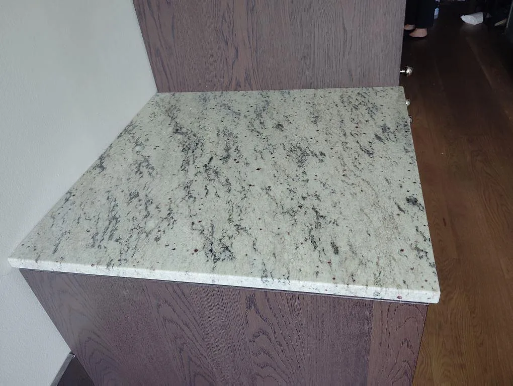 Separat träfrontad bänk med polerad Antique White granit och tydlig mörk ådring i ett kök i Lidingö.