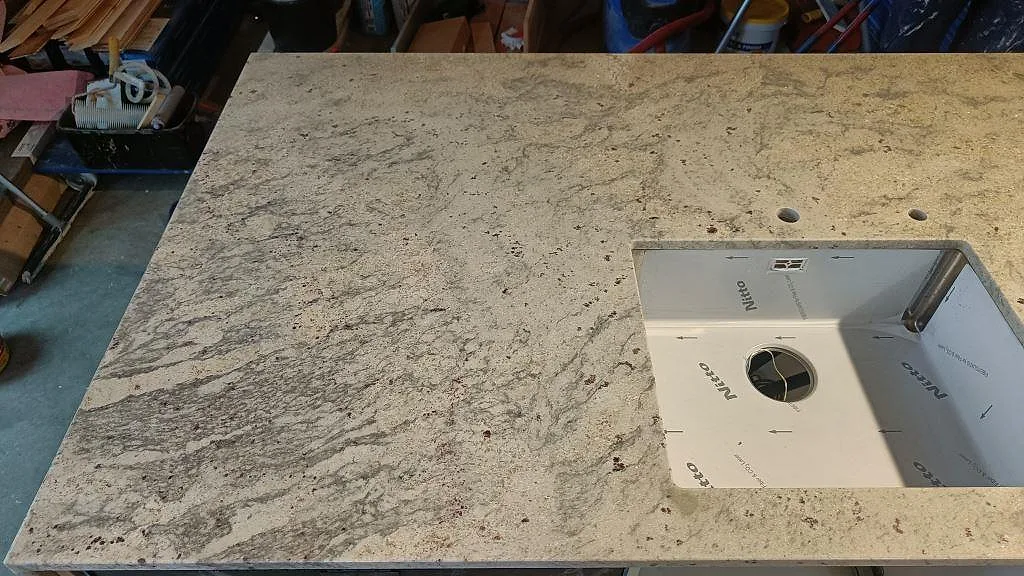 Bänkskiva i Antique White-granit med underlimmad diskhocutout, sedd ovanifrån, för ett kök i Ljungbyhed.