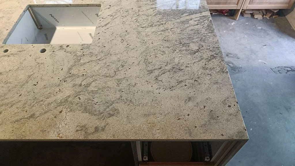 Polerad bänkskiva i Antique White-granit med underlimmad rostfri diskho i ett kök i Ljungbyhed.