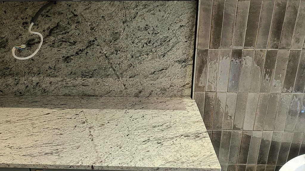 Hörn av köksbänkskiva i matt Antique White granit med stänkvägg och grå kakelvägg i Malmö.