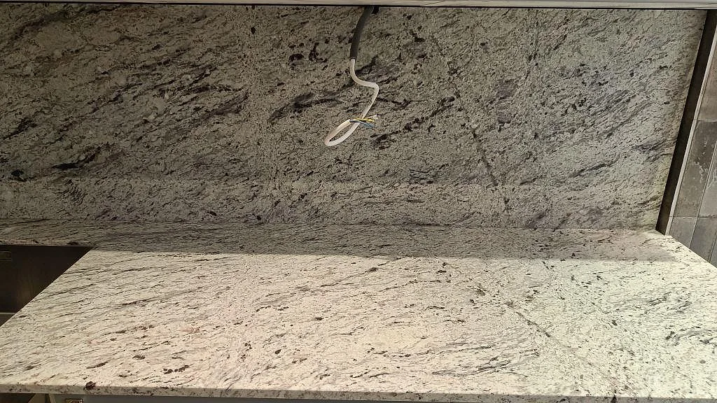 Matt Antique White granit som bänkskiva och hög stänkvägg med tydlig naturstensådring i Malmö.