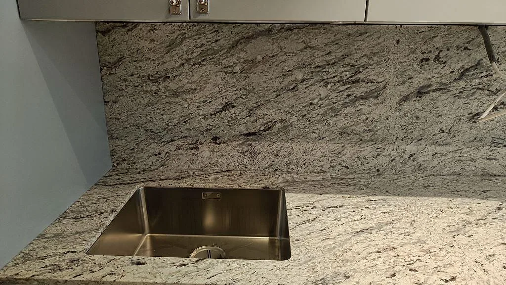 Köksbänkskiva i matt Antique White granit med underlimmad rostfri diskho och matchande stänkvägg i Malmö.