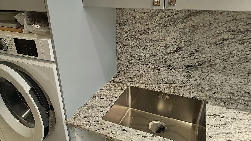 Diskhozon med matt Antique White granit, rostfri underlimmad diskho och hög stänkvägg i kök i Malmö.