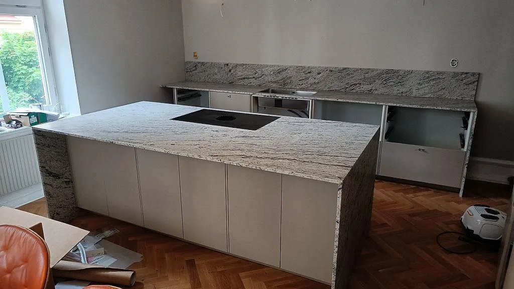 Köksö och köksbänkskiva i matt Antique White granit med svart häll och hög stänkvägg i ett kök i Malmö.