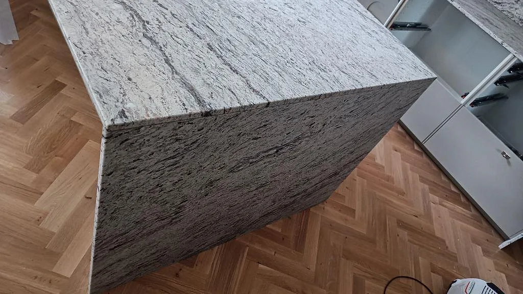 Närbild av köksö i matt Antique White granit med neddragen sida och synlig ådring i ett kök i Malmö.