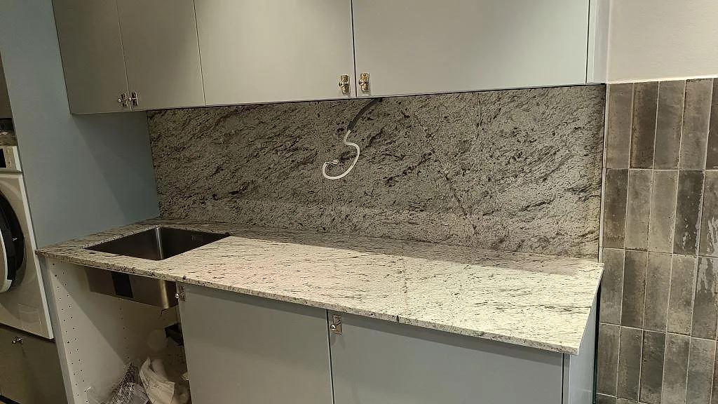 Matt köksbänkskiva i Antique White granit med rostfri diskho och hög stänkvägg under montering i Malmö.