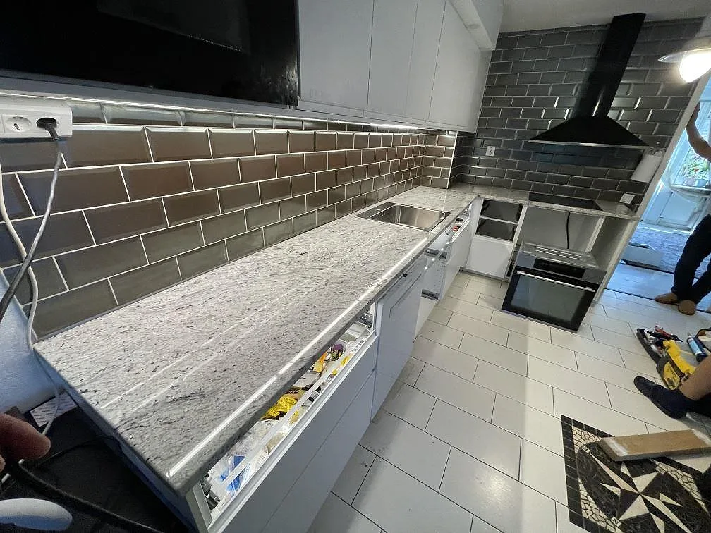L-formad köksbänkskiva i polerad Antique White granit med rostfri diskho och brungrått kakel i Malmö.