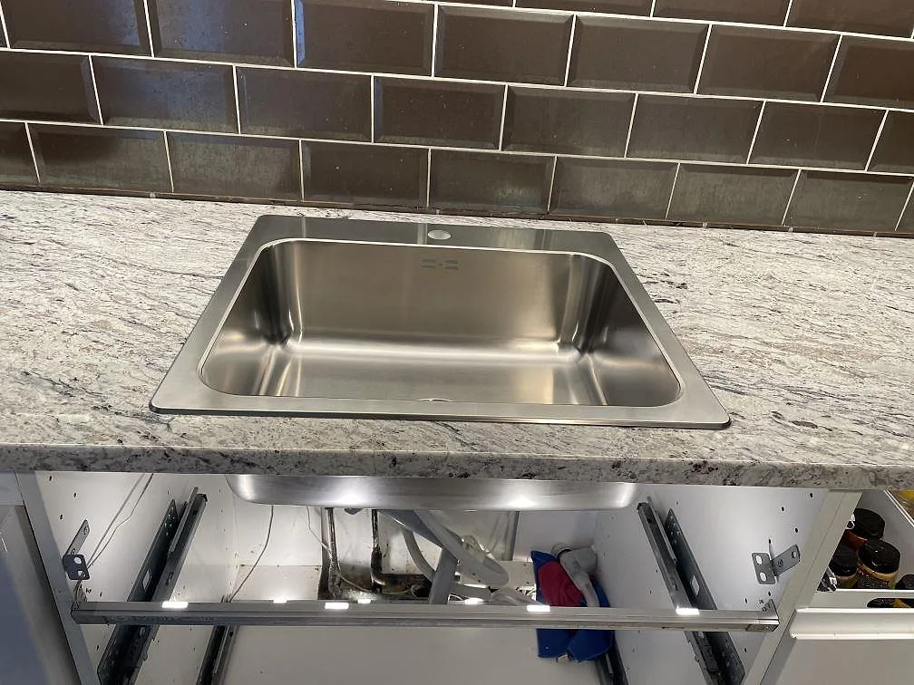 Rostfri diskho i en köksbänkskiva av polerad Antique White granit med brungrått kakel i Malmö.
