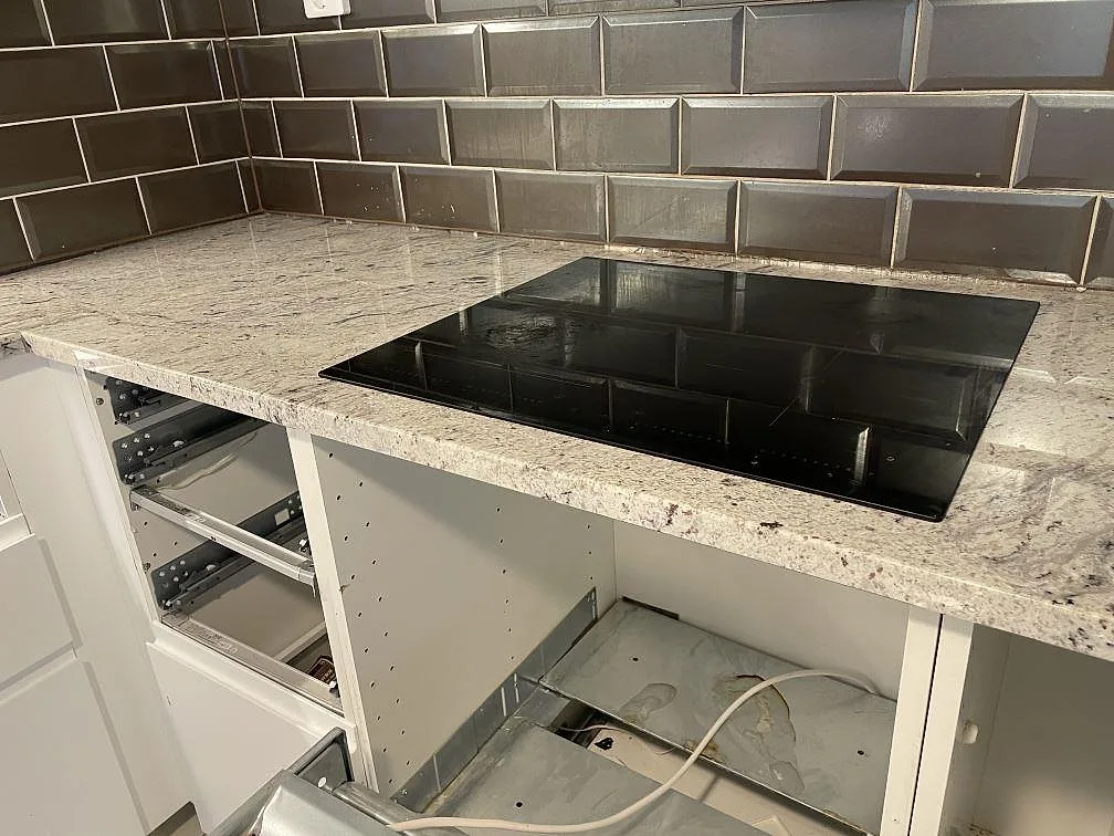 Närbild på induktionshäll infälld i polerad Antique White granit i ett kök under montering i Malmö.
