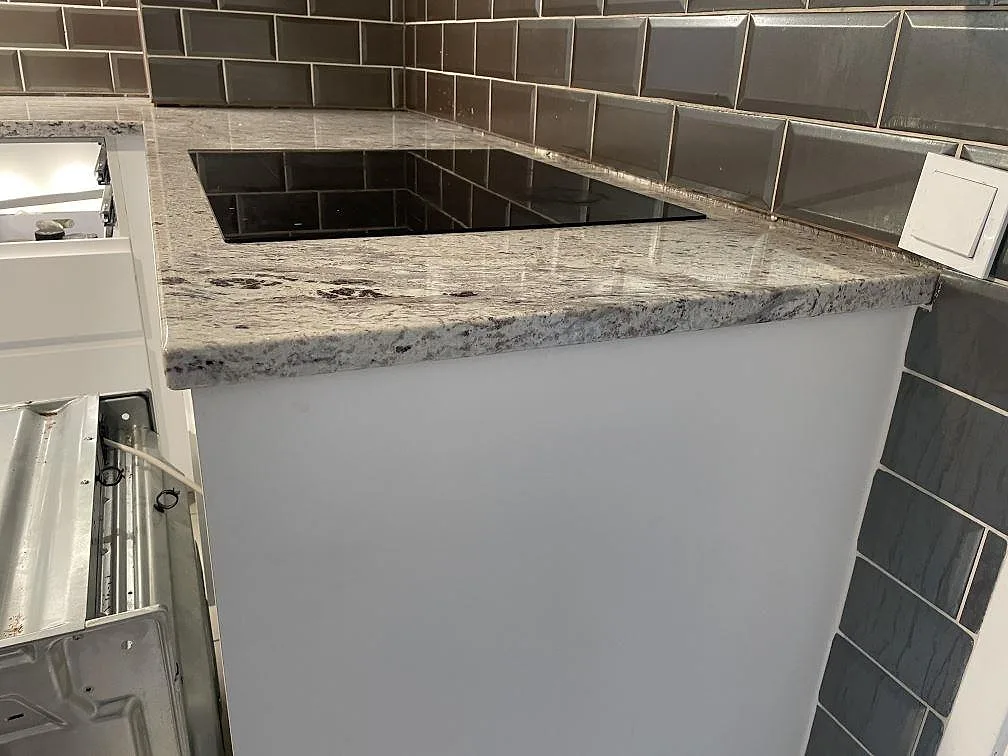 Polerad Antique White granit som köksbänkskiva runt en svart induktionshäll i ett kaklat kök i Malmö.
