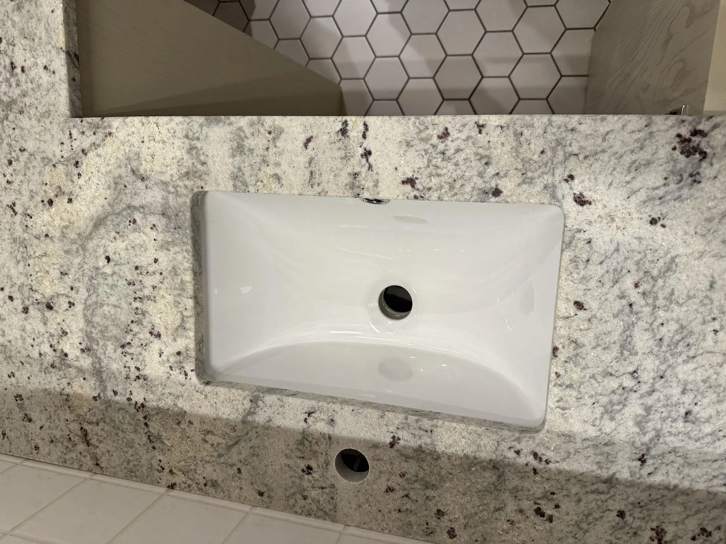 Närbild av vit underlimmad tvättställsskål i matt Antique White granit i ett badrum i Malmö.
