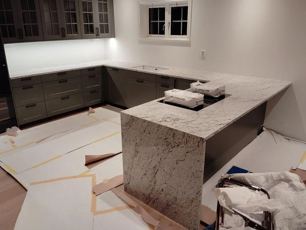 Köksbänkskiva i Antique White granit, polerad, med ljus ådring i ett U-format kök under montering i Norrtälje.