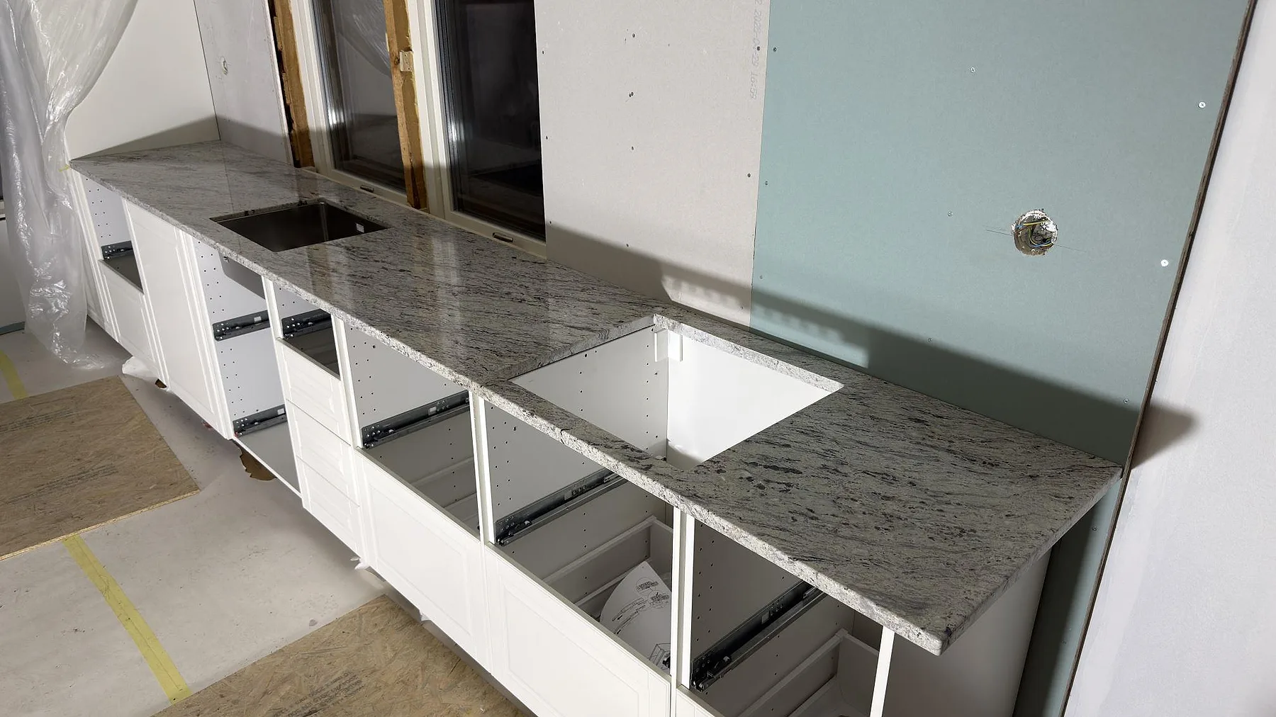 Polerad köksbänk i Antique White granit med diskhourtag och ett stänkskydd i glas, sett från sidan i ett kök i Norrtälje.