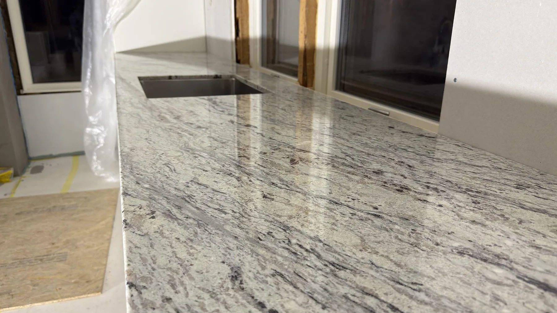 Närbild på den polerade ytan och den grå ådringen i Antique White granit vid diskhourtaget i ett kök i Norrtälje.
