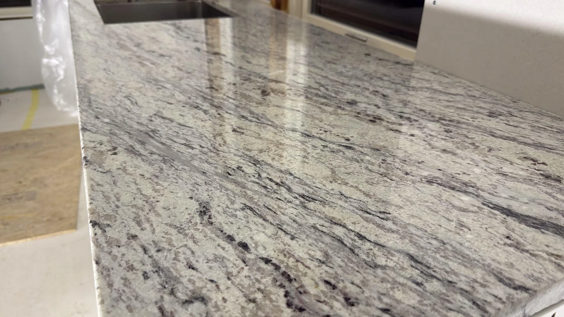 Detalj av polerad Antique White granit som speglar ljuset och visar stenens svartgrå ådring i ett kök i Norrtälje.