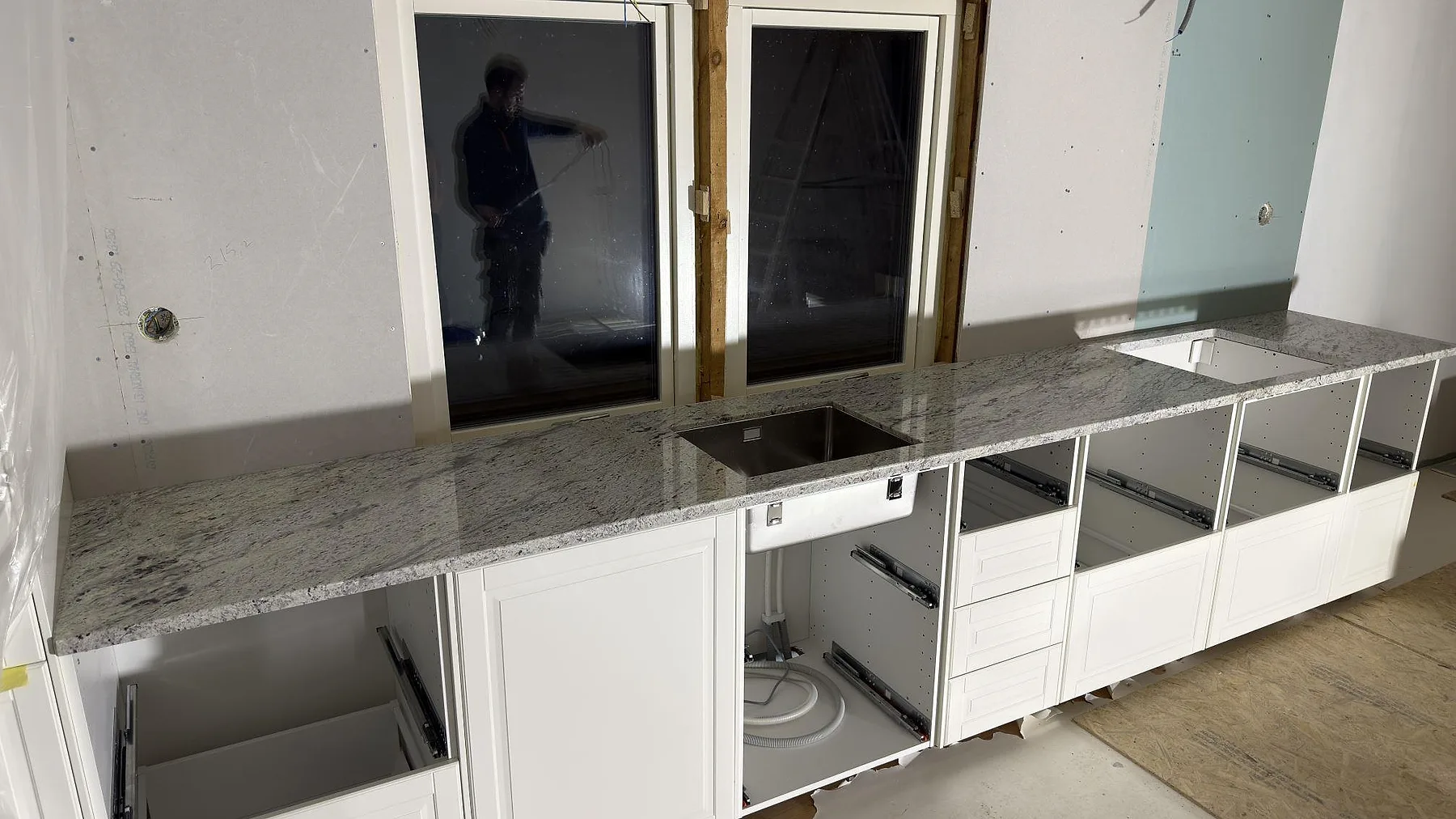 Köksbänkskiva i Antique White, polerad granit, längs en lång vägg med urtag för underlimmad diskho och häll i ett kök i Norrtälje.