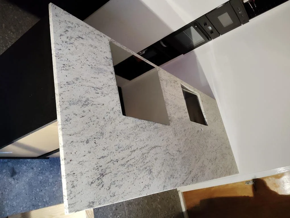 Köksbänkskiva i matt Antique White granit med synliga urtag på en kökshalvö i Saltsjöbaden.