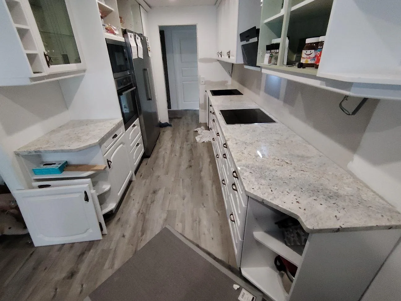 Köksbänkskiva i polerad Antique White granit, 30 mm, med diskzon och mörk häll i ett vitt parallellkök i Skärblacka.