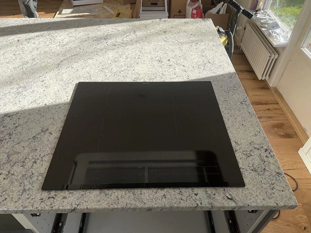 Köksö i Antique White granit med infälld svart induktionshäll, polerad yta, i ett kök i Skanör.