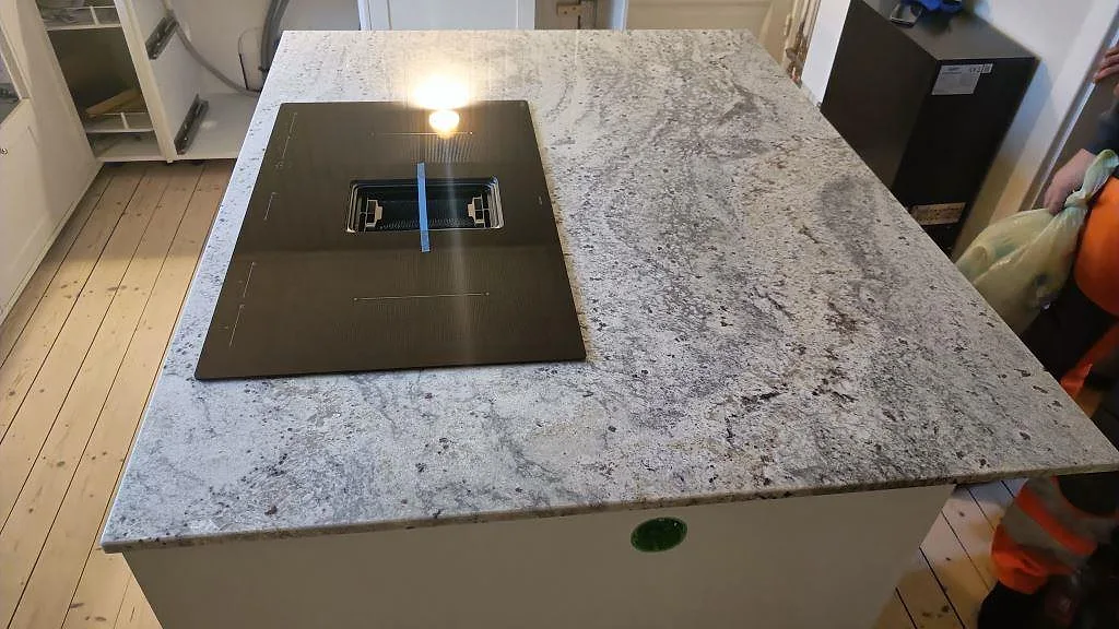 Köksö i polerad Antique White granit med svart häll och tydlig stenstruktur i Sölvesborg.