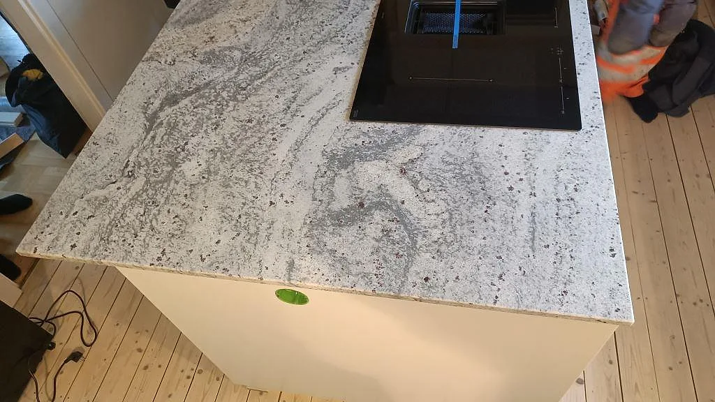 Köksö i polerad Antique White granit med häll och vit stomme under montering i Sölvesborg.