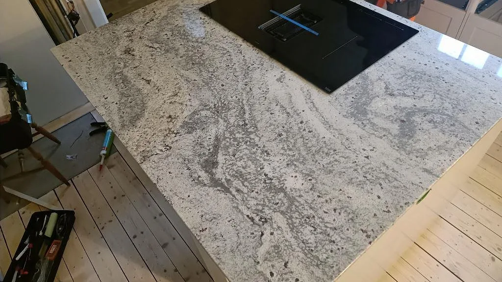 Ytbild av polerad Antique White granit på köksö med grå ådring och mörka mineralfläckar i Sölvesborg.