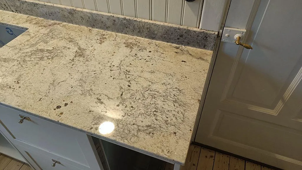 Polerad Antique White granit som bänkskiva vid dörr med uppvikt stänkkant i ett kök i Sölvesborg.
