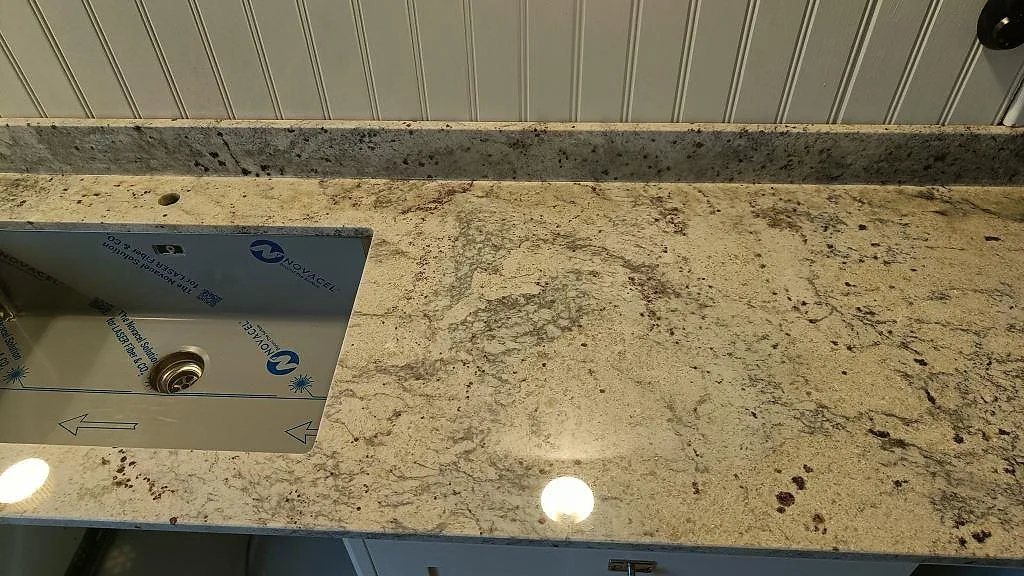Närbild av polerad Antique White granit med underlimmad diskho och stänkkant vid panelvägg i Sölvesborg.