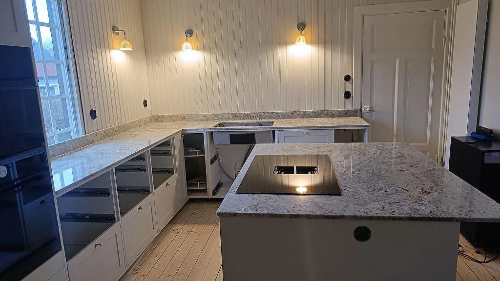 Köksbänkskiva i polerad Antique White granit med köksö, häll och bänkrader i ett kök i Sölvesborg.