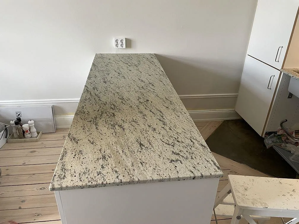 Köksö med bänkskiva i Antique White granit, matt, med ljus stenbild och mörk ådring i ett kök i Stockholm.