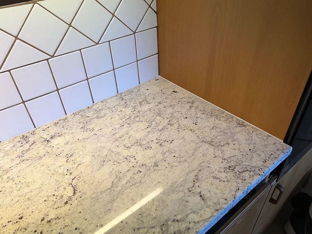 Närbild av polerad Antique White granit med ljus botten och mörka mineralpunkter i kök i Svedala.