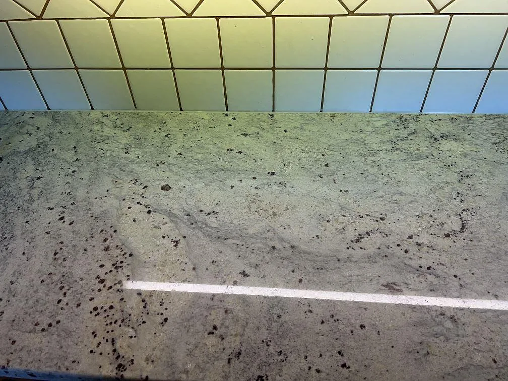 Polerad arbetsyta i Antique White granit framför vitt kvadratiskt kakel i ett kök i Svedala.